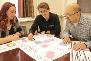 Three people working on a chart in a strategic planning meeting.